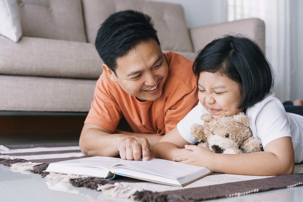 image d'un père et sa fille en train de sourire en regardant un livre
